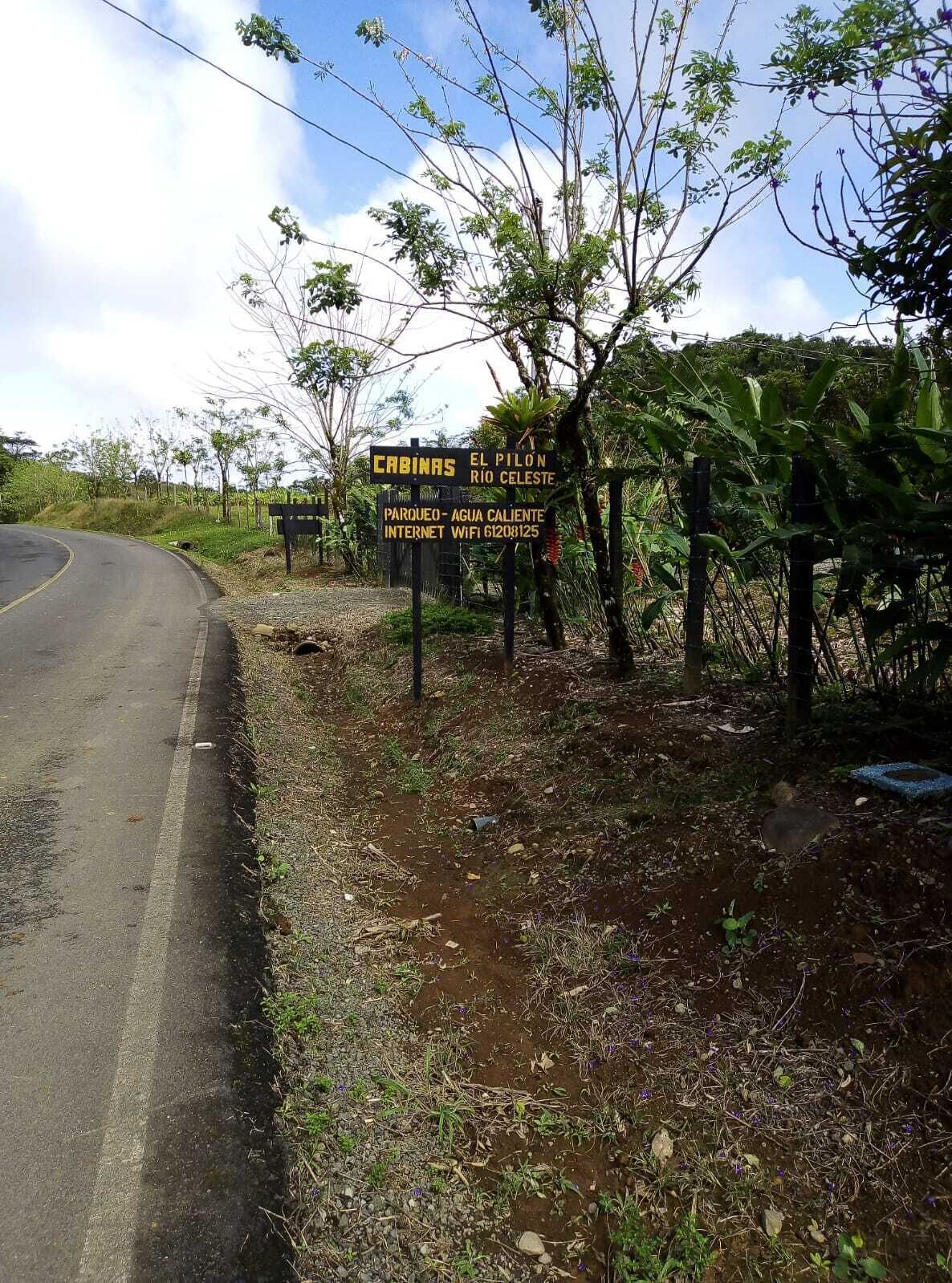 A signboard with text indicating 'CABINAS EL PILON RIO CELESTE' and 'PARKUEO-AGUA CALIENTE INTERNET WIFI 61208125'.