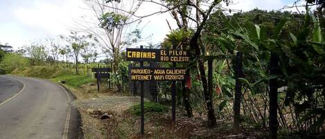 A signboard with text indicating 'CABINAS EL PILON RIO CELESTE' and 'PARKUEO-AGUA CALIENTE INTERNET WIFI 61208125'.