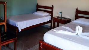 A room with two wooden beds, a wooden chair, a small bedside table with a lamp, and an air conditioning unit on the wall. - Cabinas El Pilon Rio Celeste (Katira)