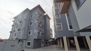 Um edifício residencial com vários andares, varandas, área de estacionamento coberta e entrada com portão.