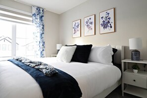 Een moderne hotelkamer met een groot bed, een nachtkastje met een lamp en drie ingelijste bloemkunstwerken aan de muur.