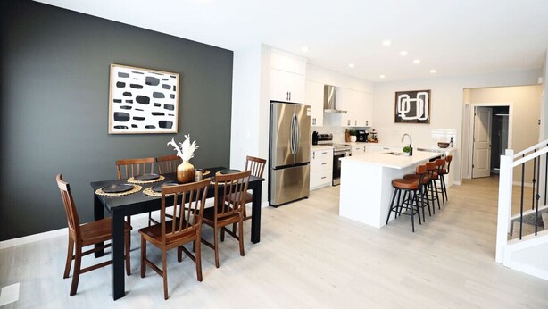 Een moderne keuken met een centraal eiland, roestvrijstalen apparatuur en een eethoek met houten stoelen en een donkere tafel.