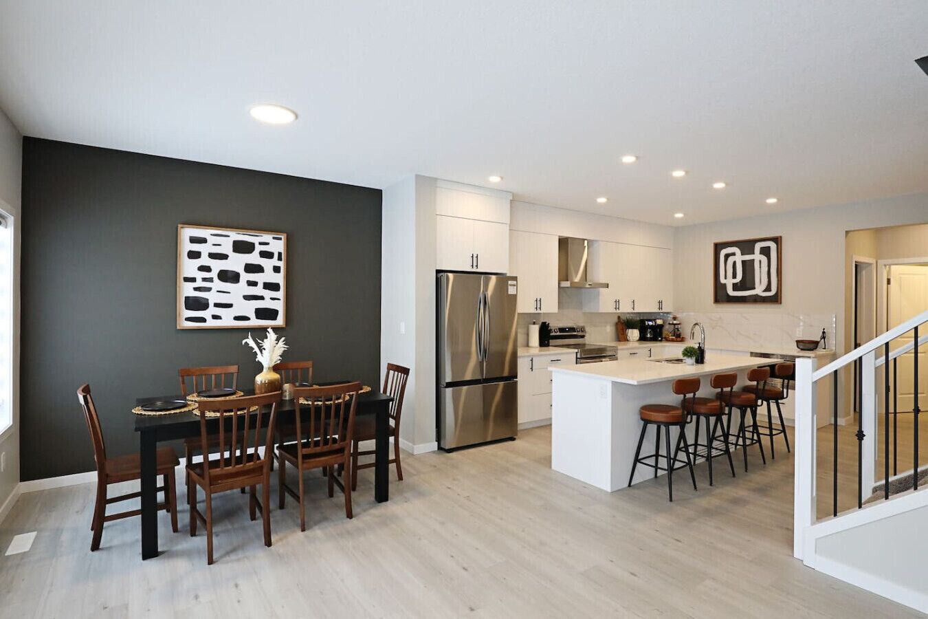A modern kitchen with a central island, stainless steel appliances, and a dining area with wooden chairs.