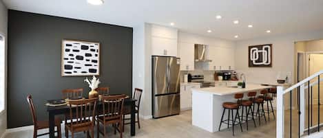 A modern kitchen with a central island, stainless steel appliances, and a dining area with wooden chairs.