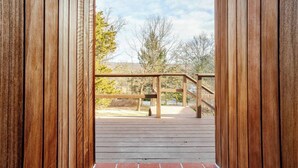 Une terrasse en bois dotée d’une rambarde, qui offre une vue sur les arbres et un ciel dégagé.