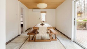 Un espace repas avec une table et des bancs en bois, un luminaire suspendu et une vue sur l’extérieur grâce à une porte coulissante.