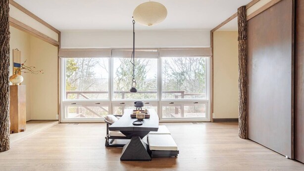 Une pièce spacieuse avec de grandes fenêtres, un plancher en bois, une table à manger avec des chaises et un luminaire suspendu.