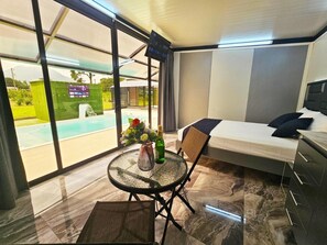 Une chambre moderne avec un lit, une petite table ornée d’un vase de fleurs et une vue sur une piscine.
