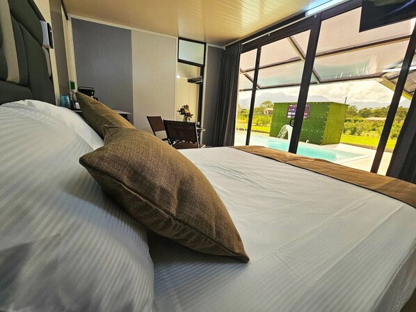 Une chambre d’hôtel avec un grand lit, une vue sur une piscine et un coin repas comprenant une table et des chaises.
