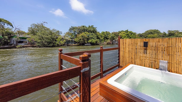 Eine Holzterrasse mit Whirlpool und Bambuszaun mit Blick auf einen Fluss.