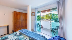Ein Schlafzimmer mit Bett, einem Holzschrank, einem kleinen Tisch und einem Balkon mit Glastür.