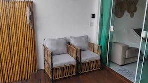 Ein Zimmer mit Holzboden, zwei Korbstühle mit grauen Kissen sowie eine Glastür zu einem Bett und einem Bambus-Raumteiler.