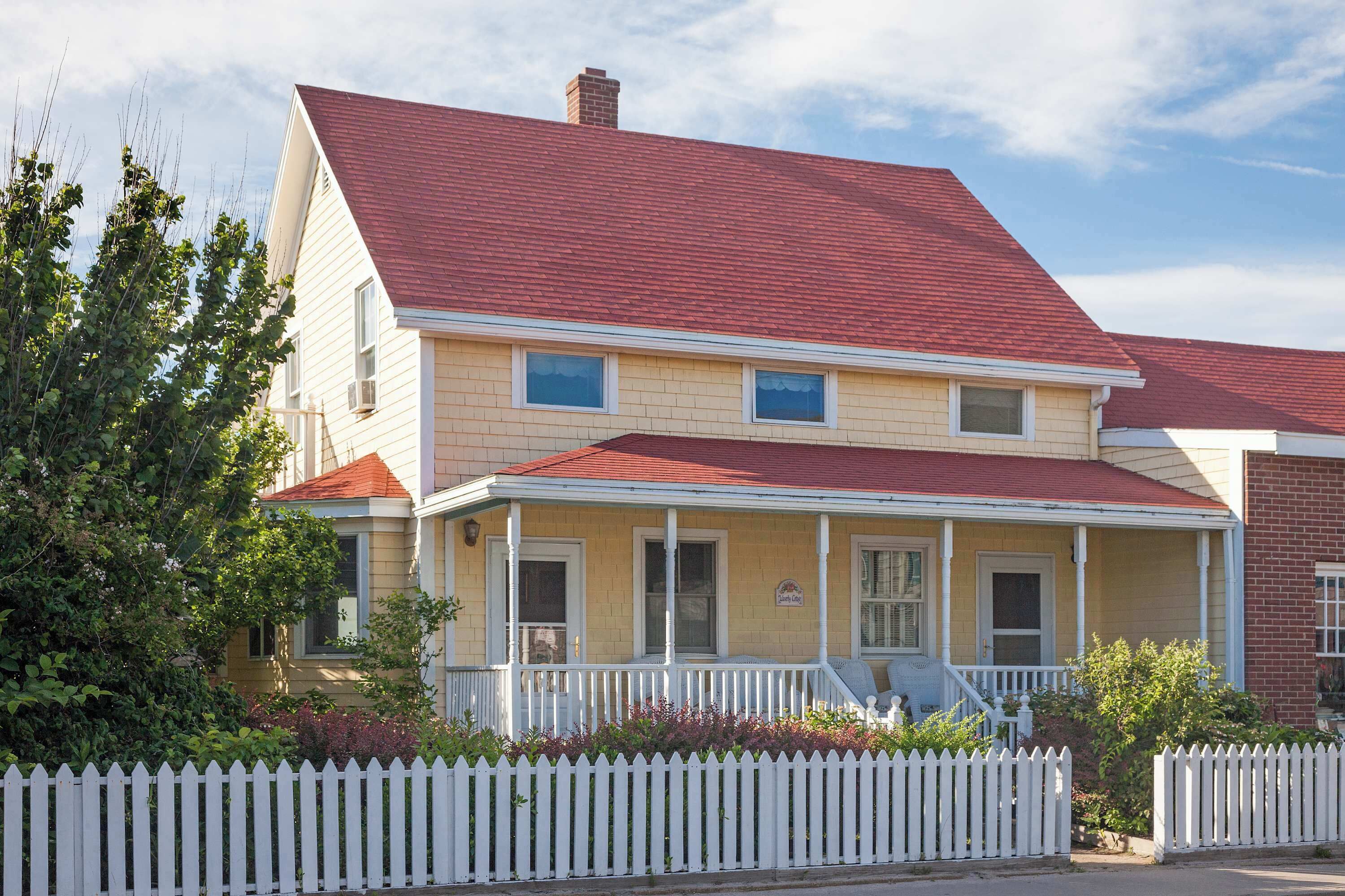 A two-story house with a red roof, white picket fence, and a porch.