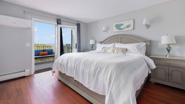 A bedroom with a large bed, a nightstand, a wall-mounted lamp, and a view of the outdoors. - Waverly Suite 2 (New Shoreham)
