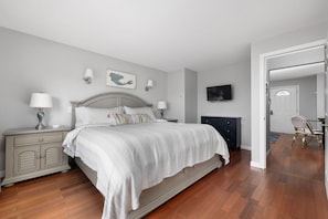 A bedroom with a bed, bedside tables, a dresser, a television, and a door leading to another room.
