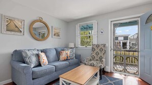 A living room with a grey sofa, a wooden coffee table, and patterned armchairs. There are framed pictures on the wall and a door leading outside. - Waverly Suite 2 (New Shoreham)