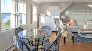 A spacious living area with a glass-top dining table surrounded by blue patterned chairs, a white sofa, and a view of the sea through large windows. - Waverly Suite 3 (New Shoreham)