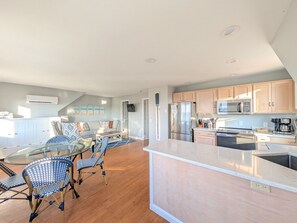 A modern kitchen with a central island, stainless steel appliances, and a dining area with a glass table and blue chairs. - Waverly Suite 3 (New Shoreham)