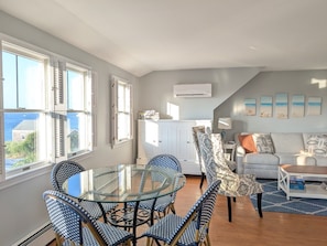 A modern living room with a glass dining table, patterned chairs, a sofa, and a view of the sea. - Waverly Suite 3 (New Shoreham)