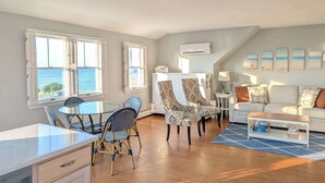 A spacious living area with a dining table and chairs, a sofa, and a view of the sea through large windows. - Waverly Suite 3 (New Shoreham)