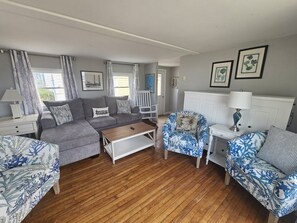 A living room with a grey sofa, a patterned armchair, a wooden coffee table, and a white side table with a lamp. - Sherman Cottage (New Shoreham)