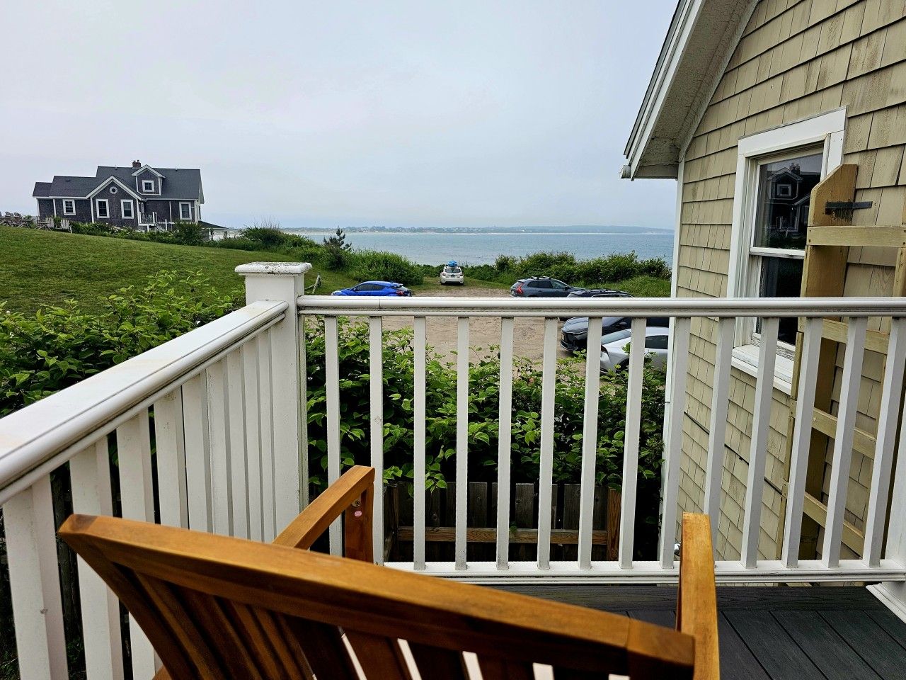 A balcony with a view of the sea, a wooden chair, and a white railing.