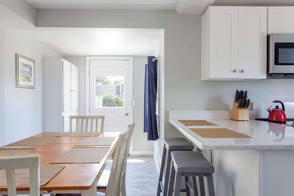 Una cocina moderna con armarios blancos, un microondas y una tetera roja sobre la encimera.