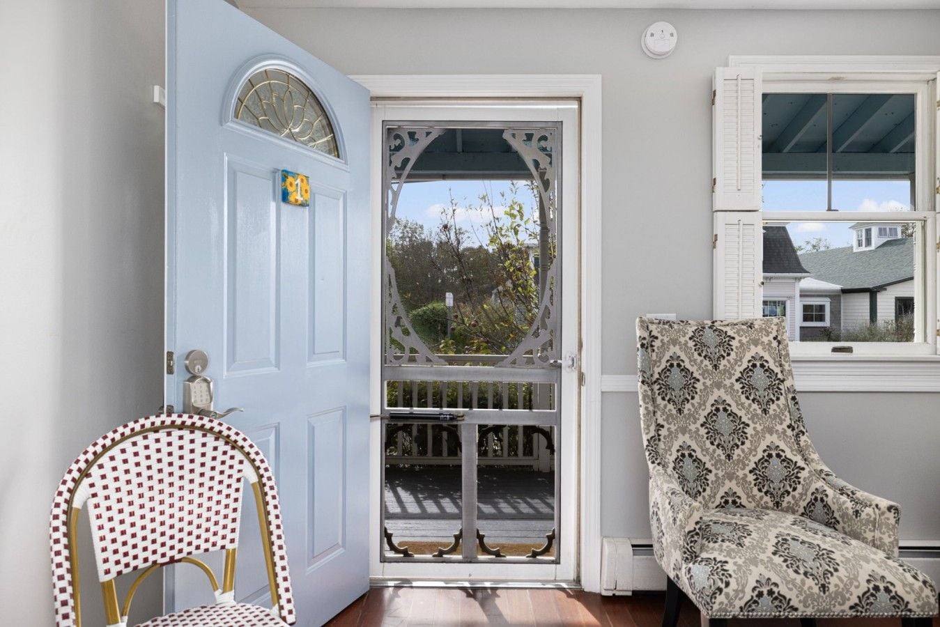 A room with a blue door, a patterned armchair, and a chair with a checkered cushion.