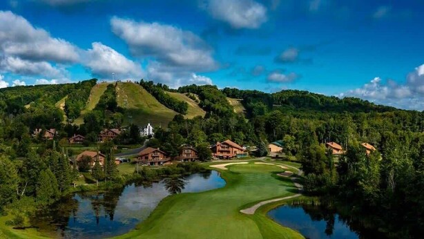 Un campo de golf con un estanque, rodeado de casas y una colina con un edificio en la cima.
