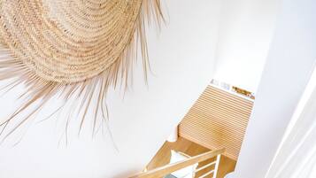 Una escalera de madera con barandillas blancas, un techo tejido colgante, y vista a una habitación con piso de madera y una ventana.