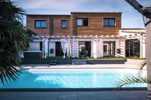 Una casa moderna con piscina, fachada de madera y un patio cubierto.