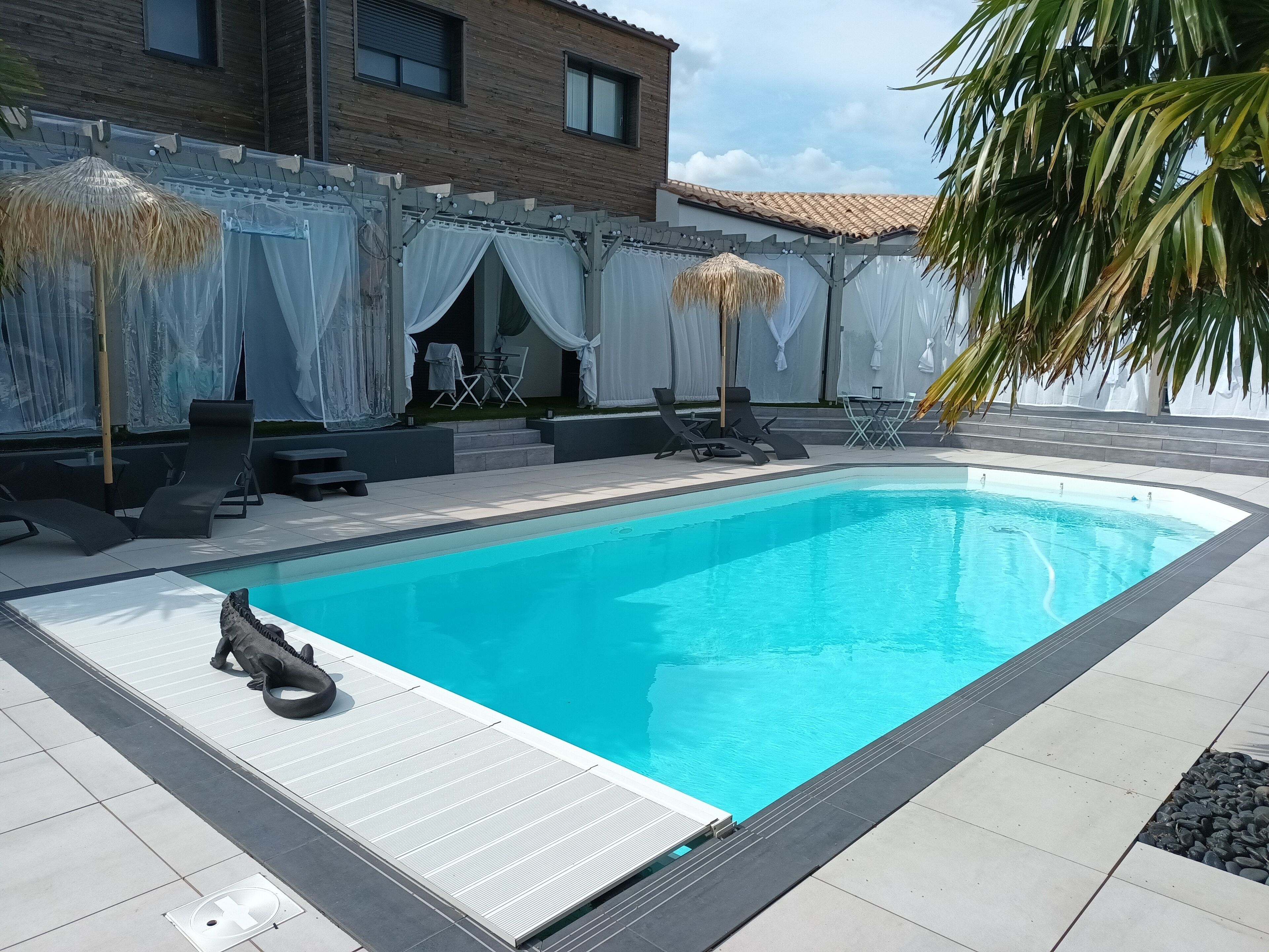 A swimming pool with lounge chairs and a covered seating area.
