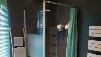 Een moderne badkamer met een douchecabine van glas, een houten trapje, een handdoekhouder en een wit opbergmeubel.