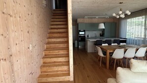 Un interior moderno con una escalera de madera que lleva a una zona de cocina, una mesa de comedor con sillas y un sofá.