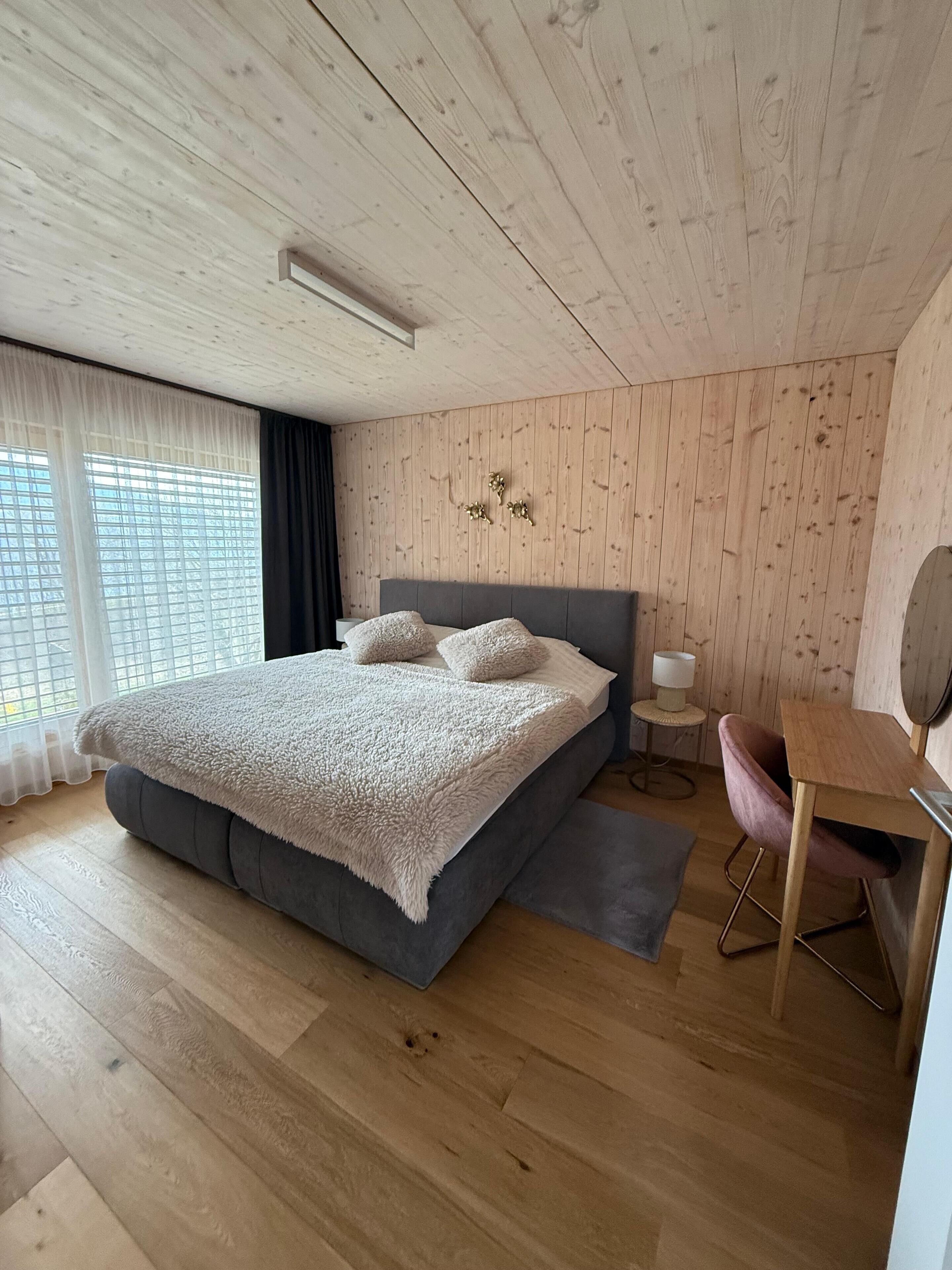 Un dormitorio moderno con una cama grande, un escritorio pequeño y una ventana con cortinas.