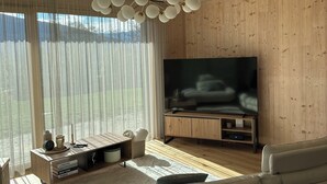 Una sala de estar moderna con un televisor de pantalla plana grande, paneles de madera, un sofá blanco y un techo de madera con una lámpara de araña original.