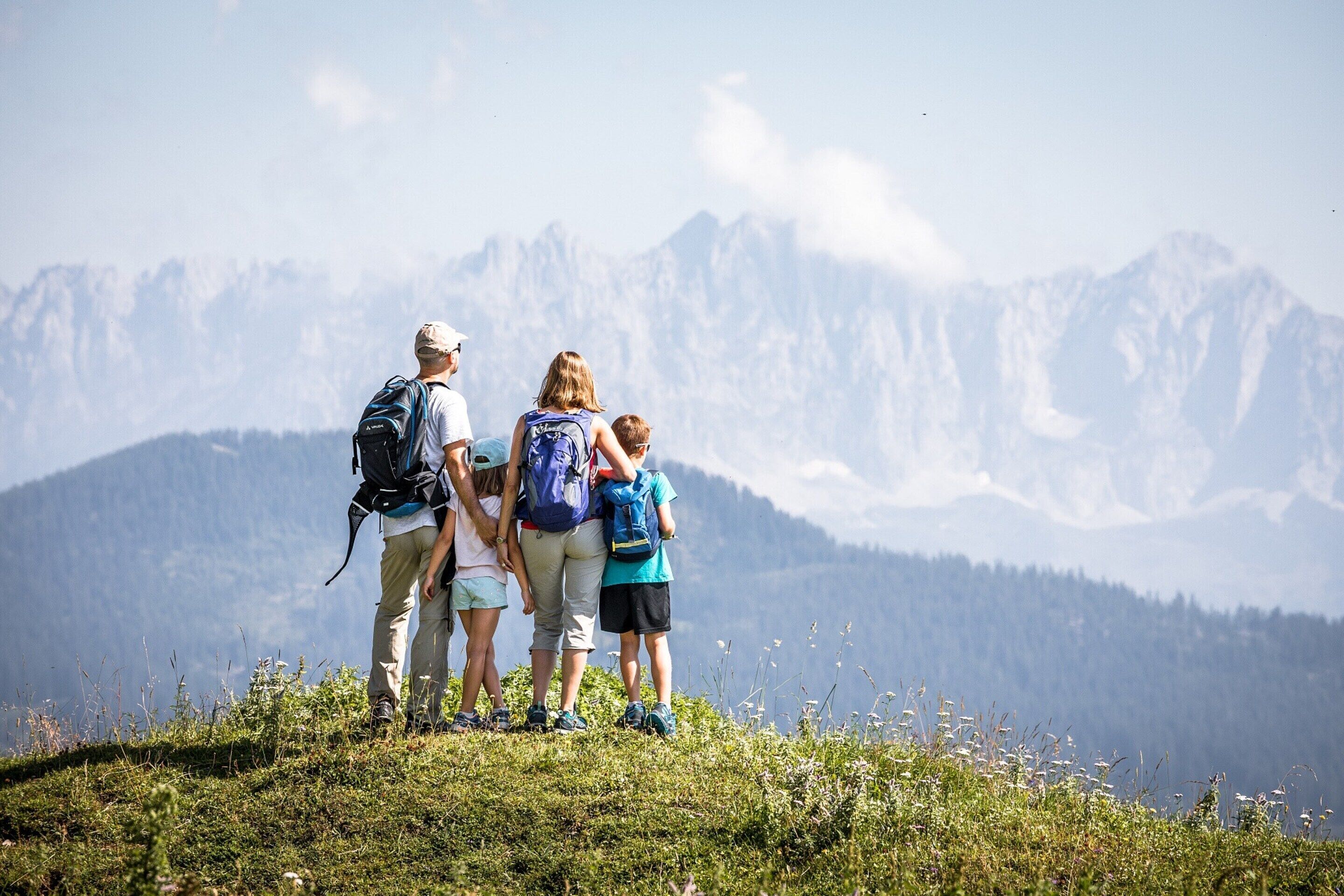 Eine vierköpfige Familie steht auf einer grünen Hügelkuppe vor einer Berglandschaft.