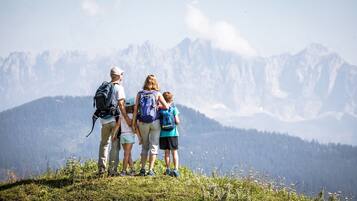 Eine vierköpfige Familie steht auf einer grünen Hügelkuppe vor einer Berglandschaft.