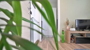 Un soggiorno moderno con pavimento in legno, una TV a schermo piatto, un vaso verde e una pianta in primo piano.