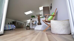 Un'ampia zona giorno con soffitto alto, pavimento in legno, un divano, una poltrona e un tavolino con una pianta.