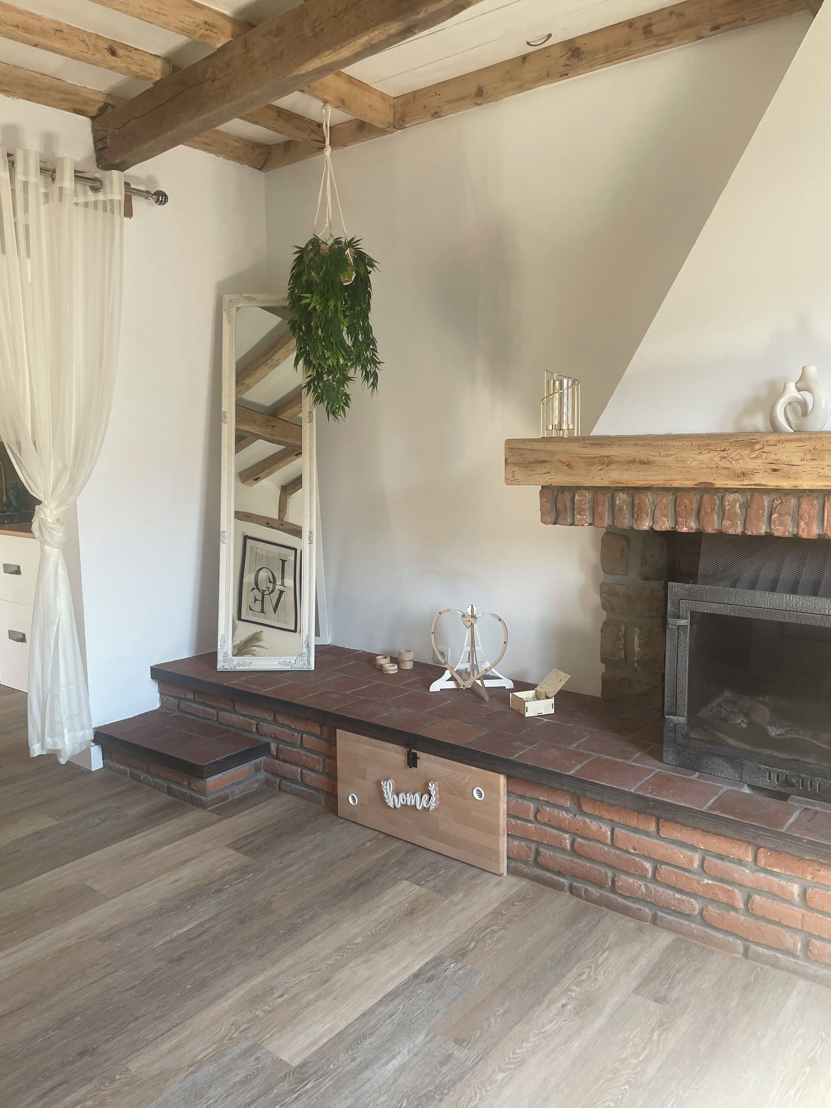 A cozy living room with a brick fireplace, wooden beams, and a hanging plant.