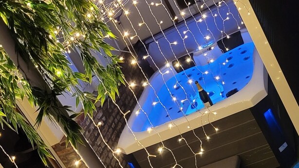 Área de piscina com hidromassagem, rodeada por luzes de corda e vegetação.