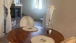 Uma mesa de jantar com duas cadeiras, um vaso com flores secas e uma lareira ao fundo.