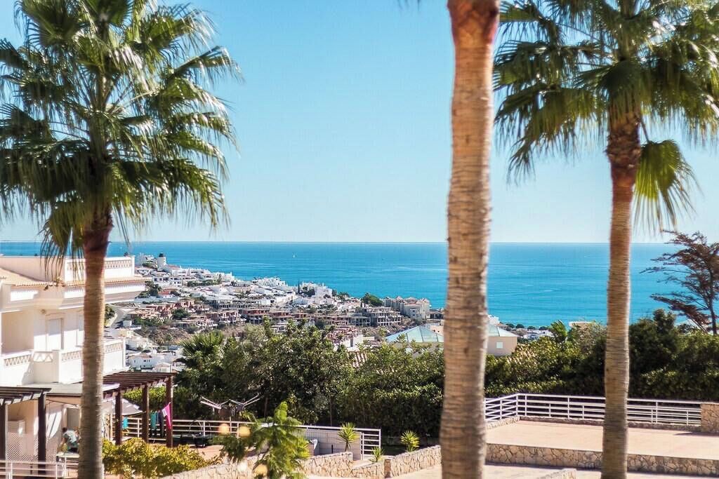A coastal town with a view of the sea, palm trees, and buildings.