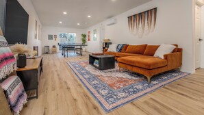 Ein geräumiges Wohnzimmer mit einem großen orangefarbenen Sofa, einem gemusterten Teppich und Holzböden.