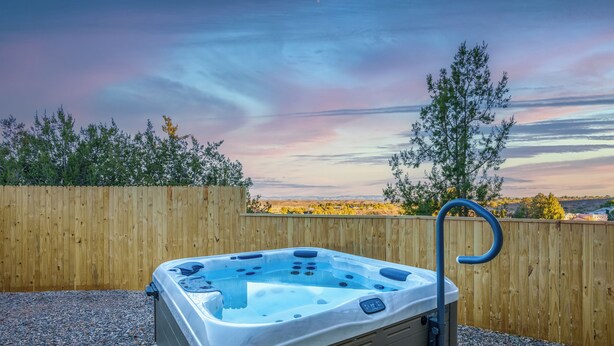 Ein Whirlpool in einer Außenanlage mit Holzzaun und Bäumen im Hintergrund.