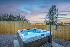 Un bain à remous installé à l’extérieur, avec une clôture en bois et des arbres en arrière-plan.