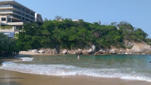 Une plage aux eaux cristallines, un rivage rocheux et un bâtiment doté de balcons.