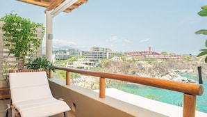 Un balcon avec un fauteuil de relaxation blanc, une balustrade en bois et une vue sur une zone balnéaire avec des bâtiments et un ciel dégagé.