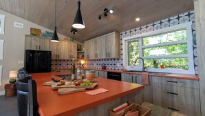 A modern kitchen with wooden cabinets, a large island, pendant lighting, and a window with a view of greenery. - Luxury Lakefront Retreat | 3 bed,3 bath, near Parry Sound | Save on Weekly Stays (Parry Sound)